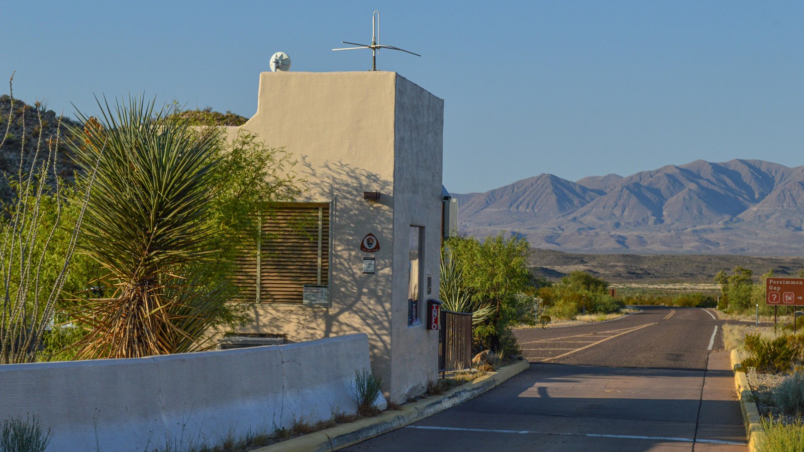 An adobe structure sitting in the middle of the highway has a window where visitors pay to enter.