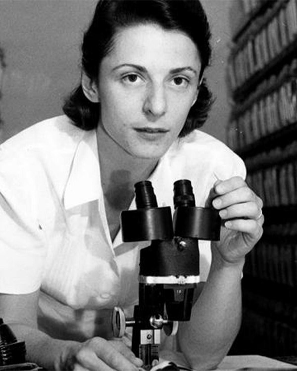 Black and white photo of a woman leaning over a microscope.