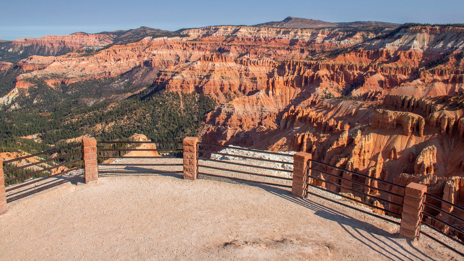 A black-tube railing surrounds a semi-level gravel area overlooking a massive rock formation.