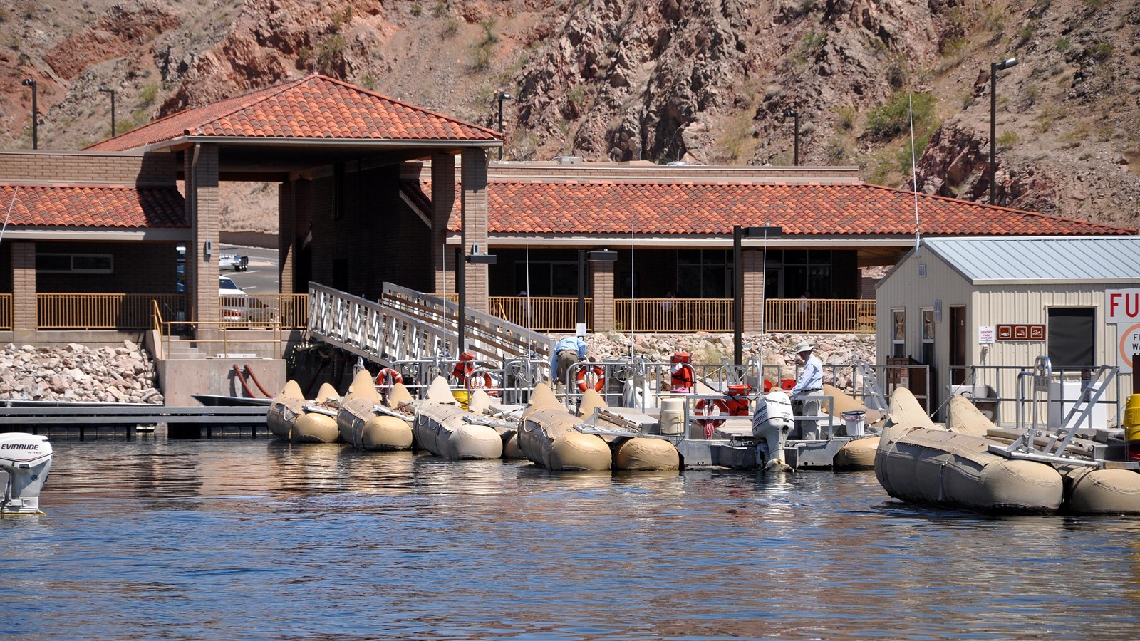 Marina with boats by a river and desert mountain.