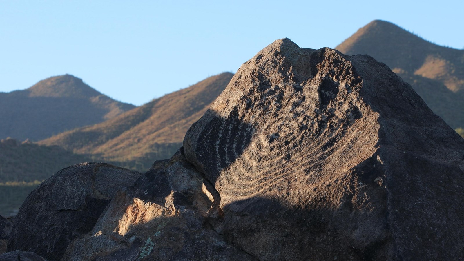 A large boulder sits in the right of the image, a large spiral image is etched into the stone.