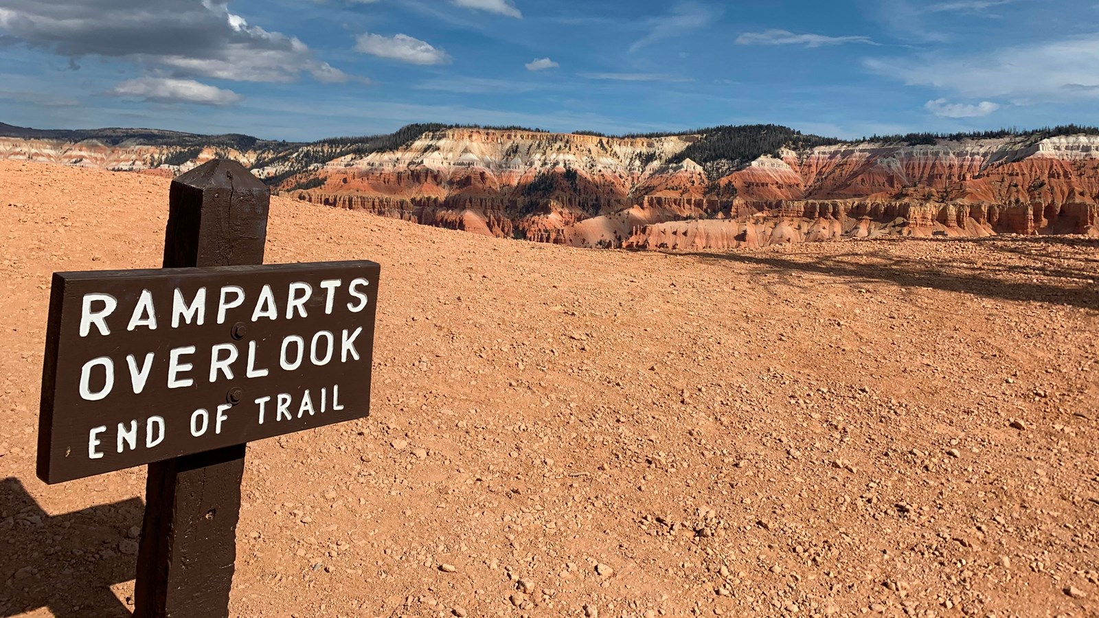 A wooden sign in the foreground reads Ramparts Overlook, rock formations are behind in the distance.