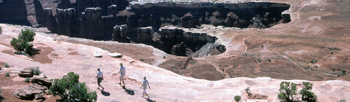 an overhead view of three people on a cliff edge with distant canyons beyond