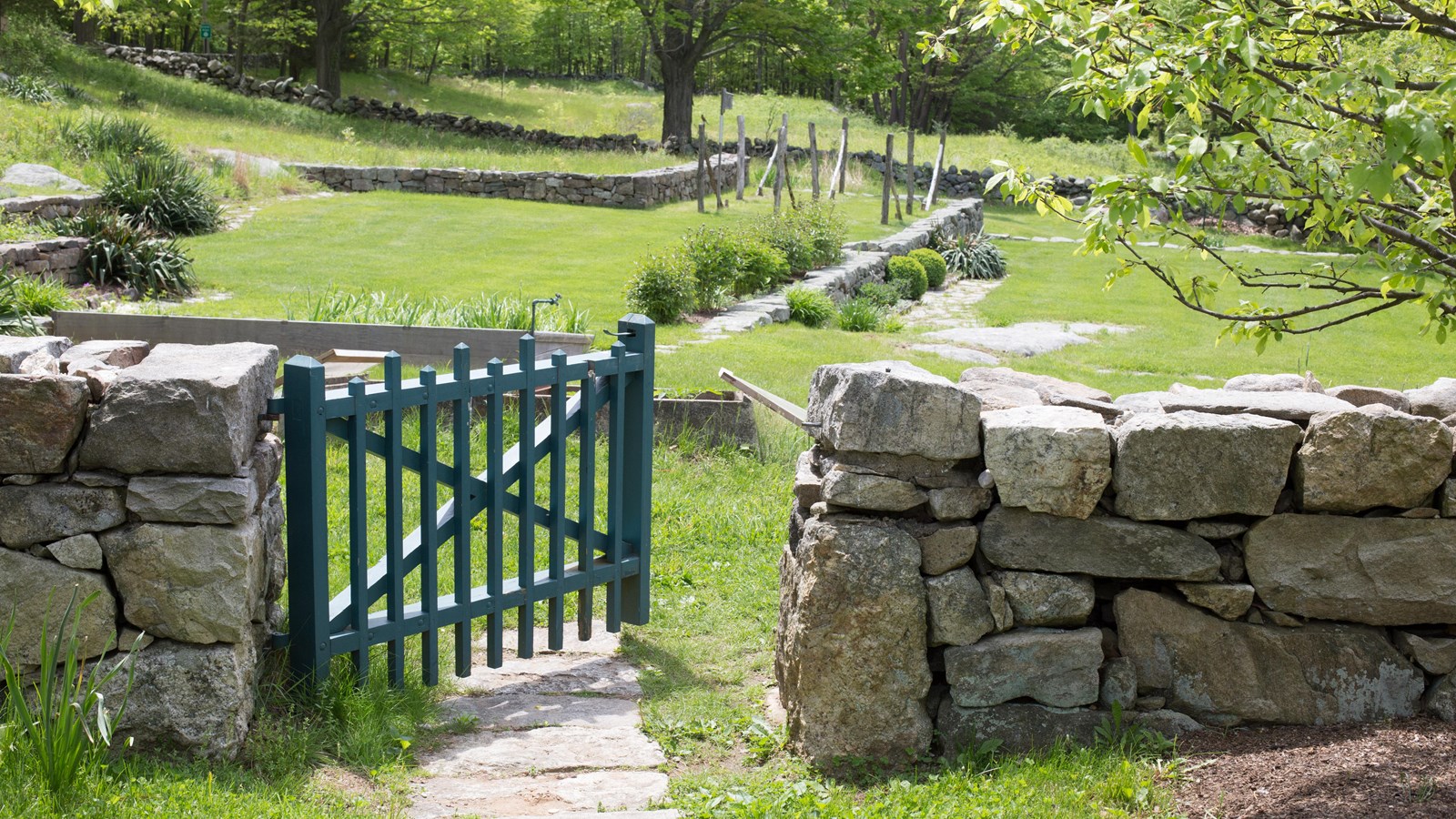 A green gate in a stone wall that leads into a grassy meadow.