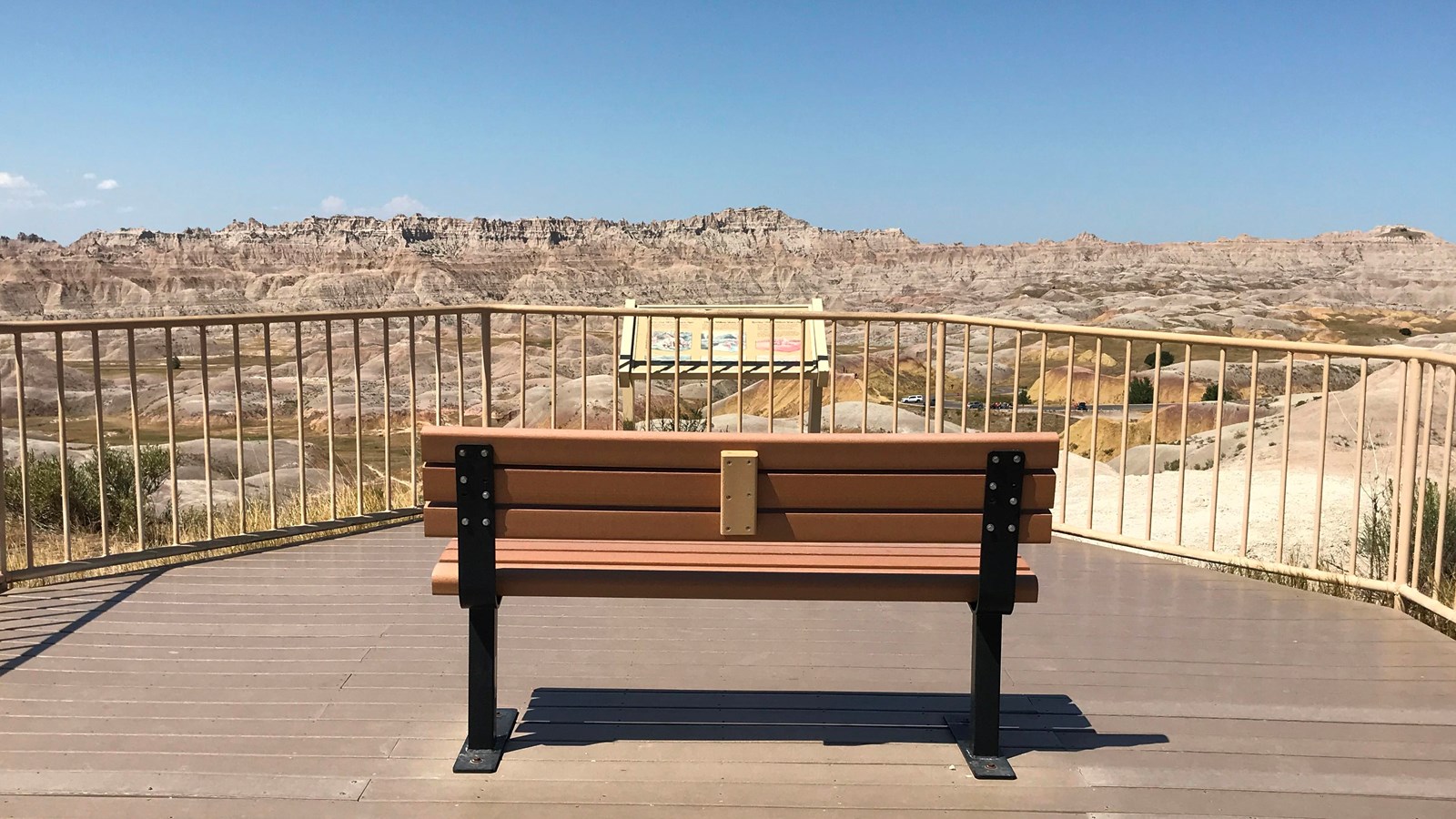 A bench on a boardwalk faces a badlands landscape extending into the horizon under a blue sky.