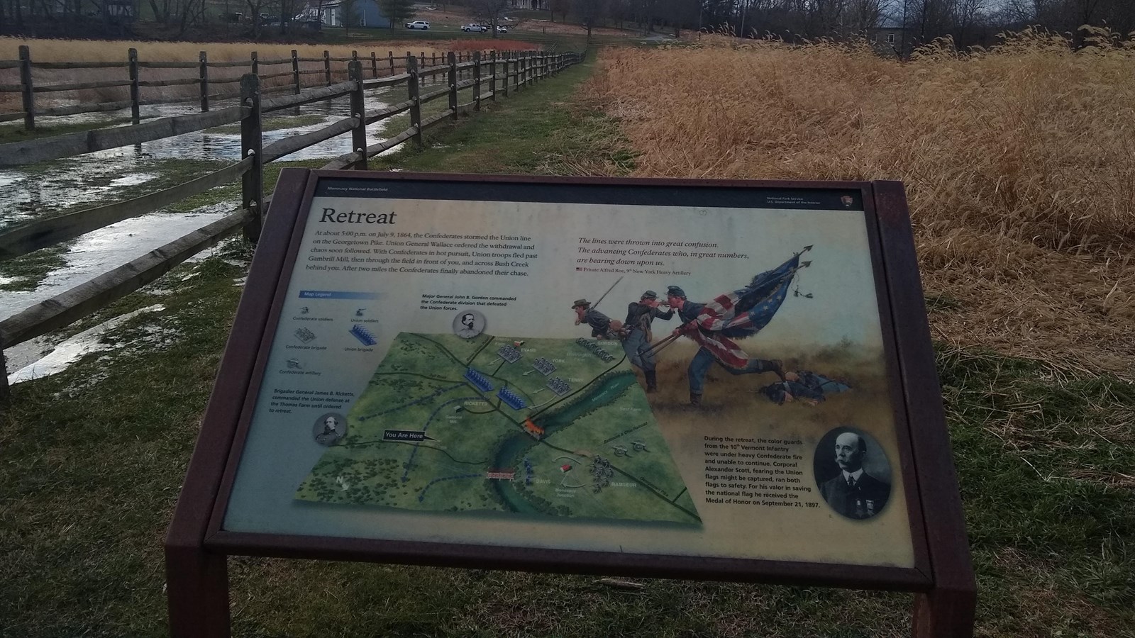 A colorful sign with illustrations and text sits at the edge of a meadow.