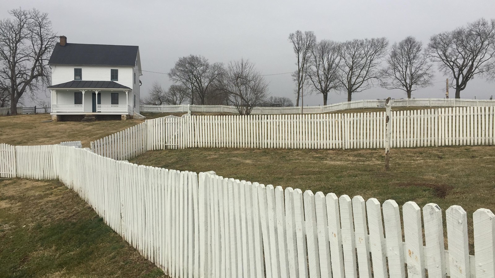 white picket fence leads to white house with black roof