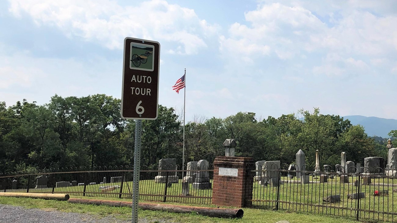 A road sign labeled auto tour 6 marks a tour stop and exhibit by a cemetery.