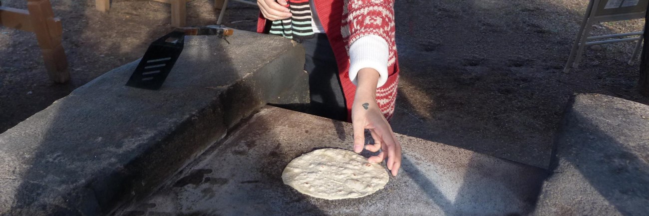 young woman flipping a flour tortilla on an open comal