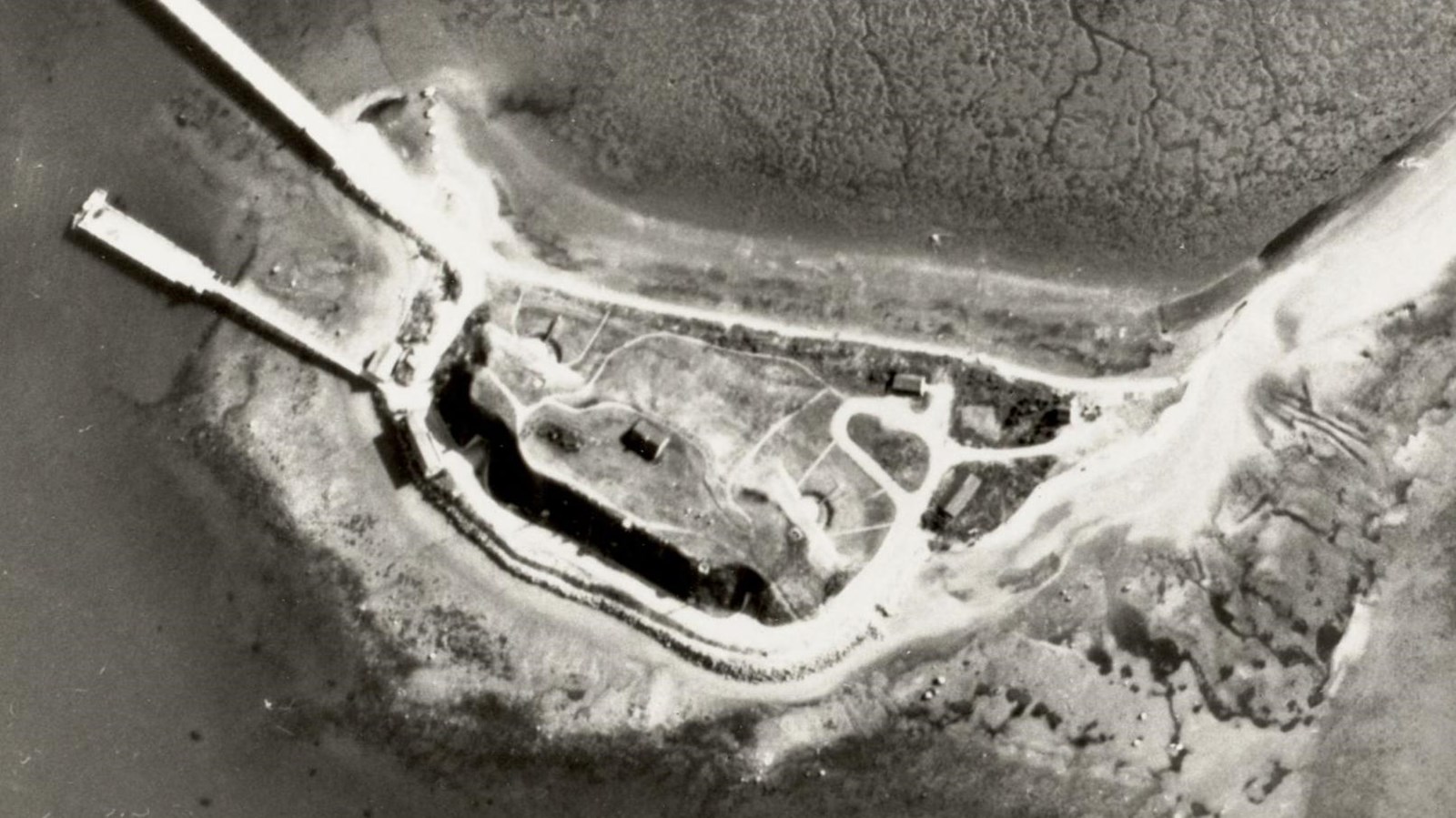 aerial shot of an island with a dock and a bridge to mainland. Buildings of a fort.