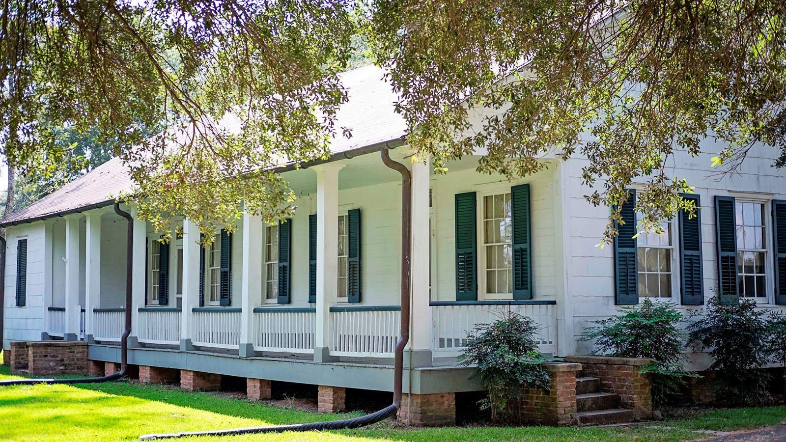 A white house with green shutters and a front porch on brick piers.