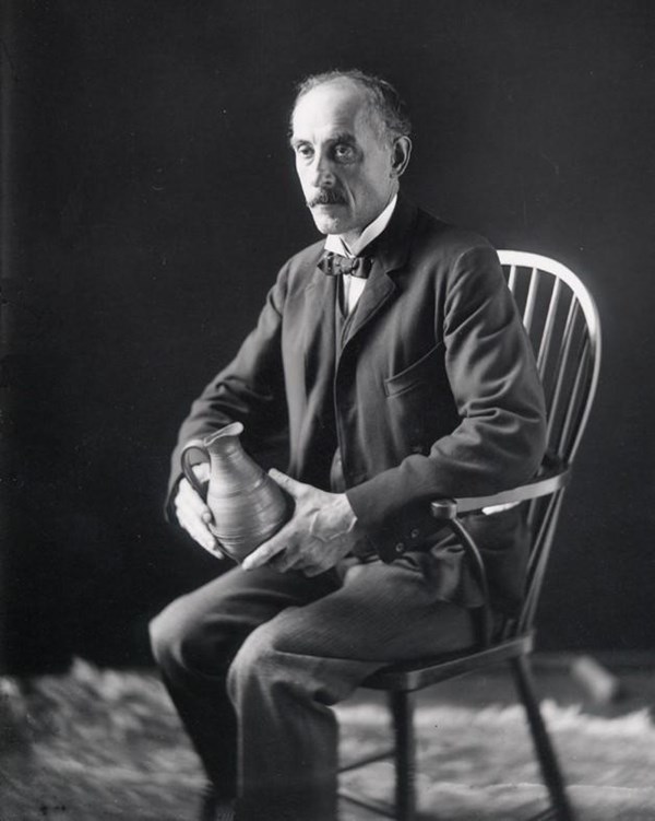 Man seated in chair holding pottery pitcher.