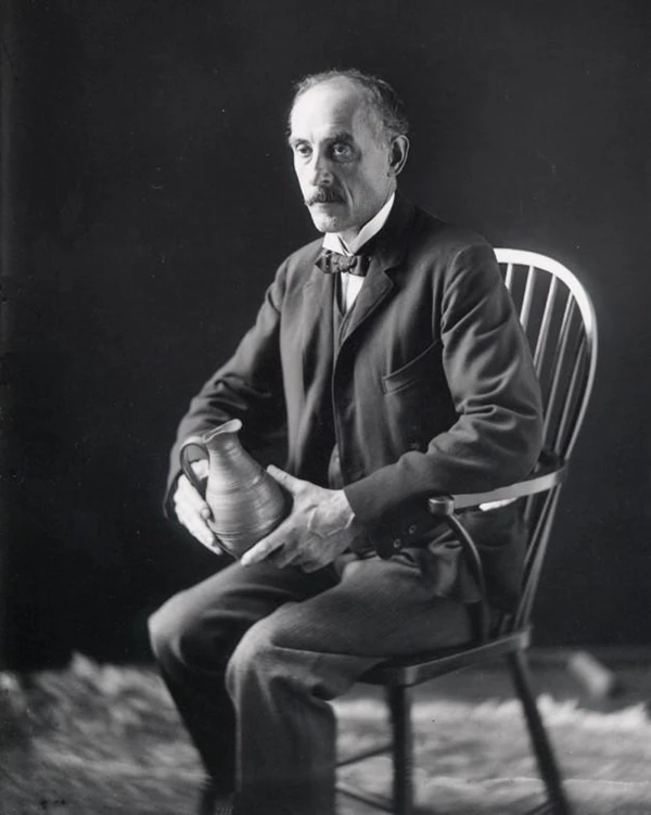 Man seated in chair holding pottery pitcher.