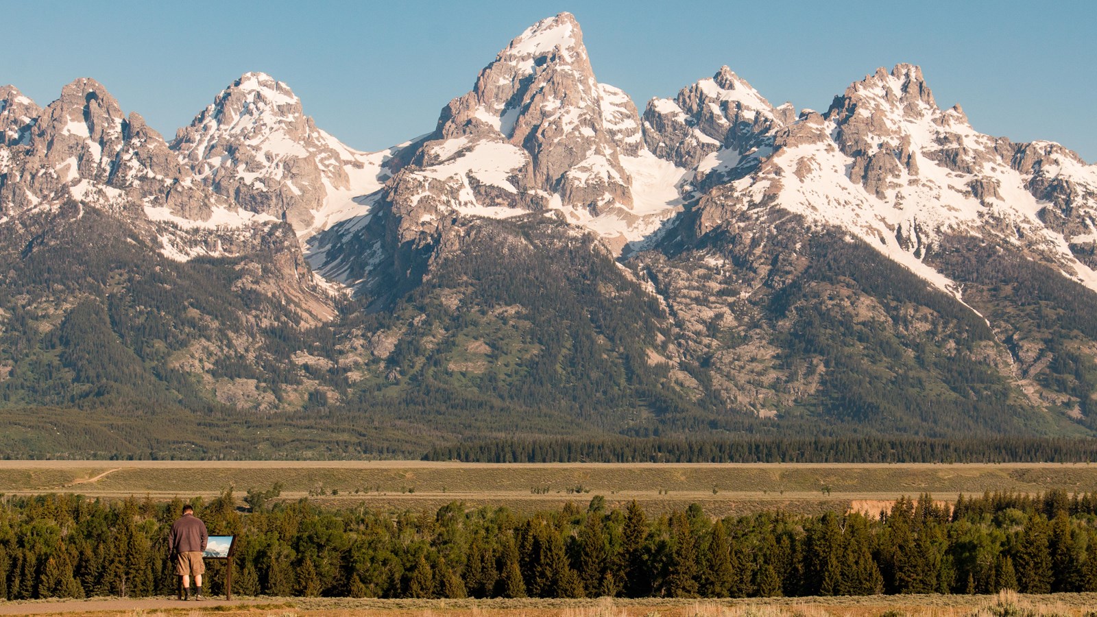A person looking at a sign with mountains in the background