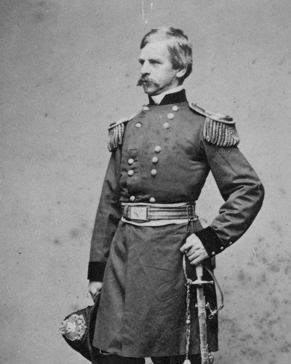 A general in 1860s military dress poses with a saber for a full-length portrait photo.
