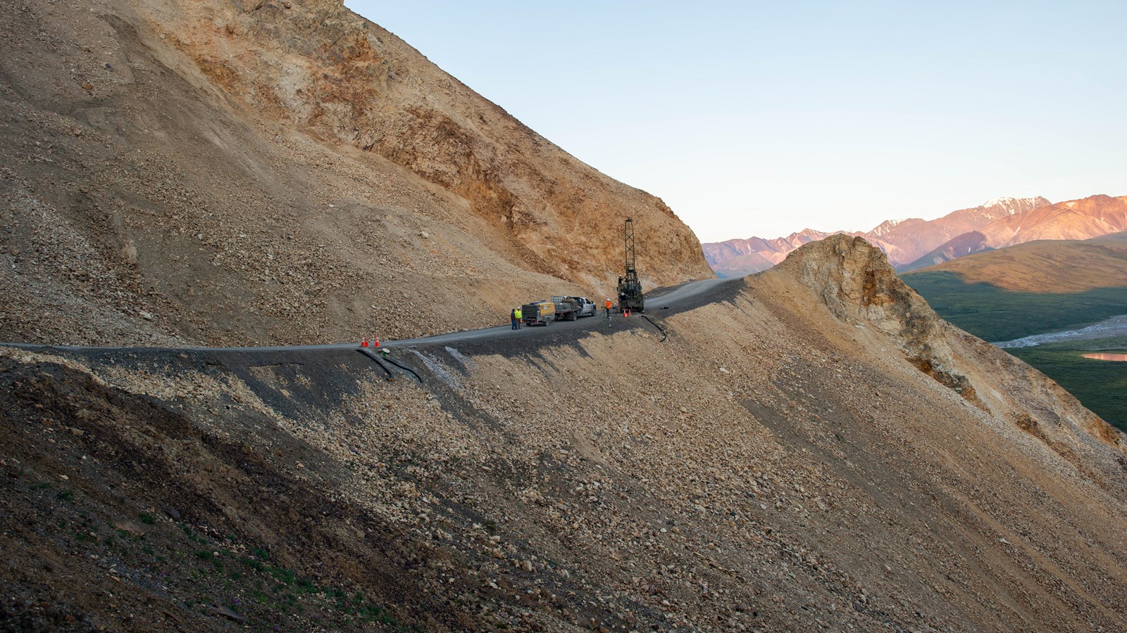 A truck and drilling equipment on a narrow road with a steep, rocky slope below.