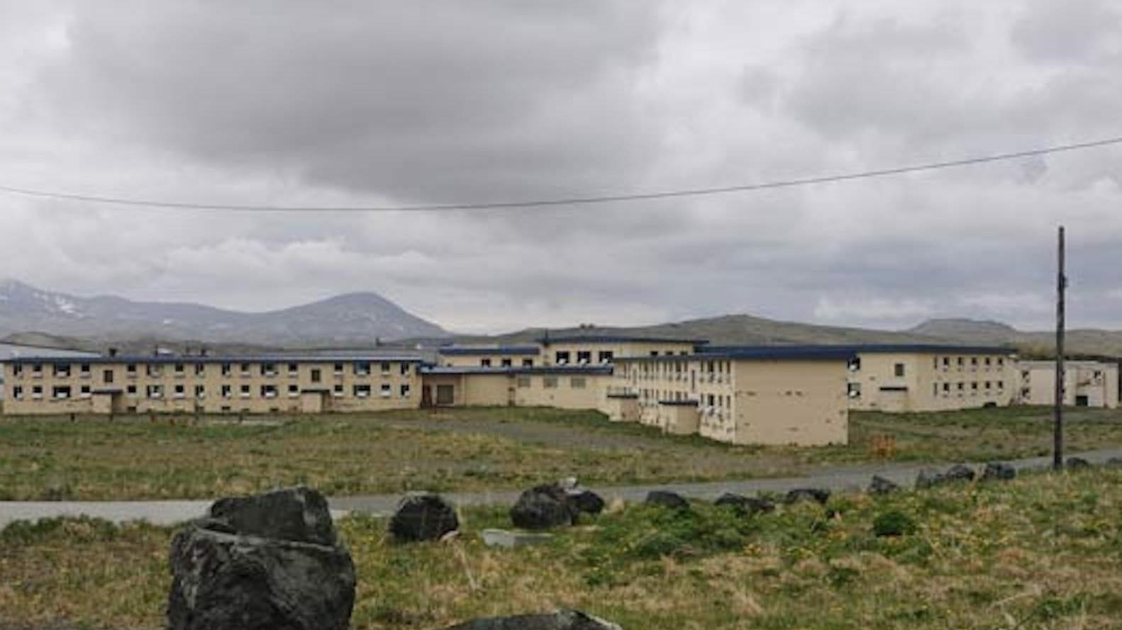 An expansive two story barracks building, on the tundra, with beige paint and a gray roof.