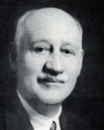 Man in suit with white hair and mustache poses for picture