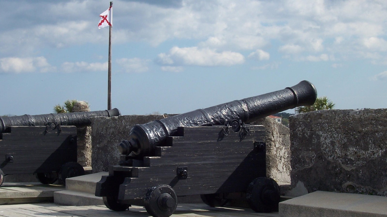 Large Iron Cannon on Carriage on wooden platform and pointing over a stone wall