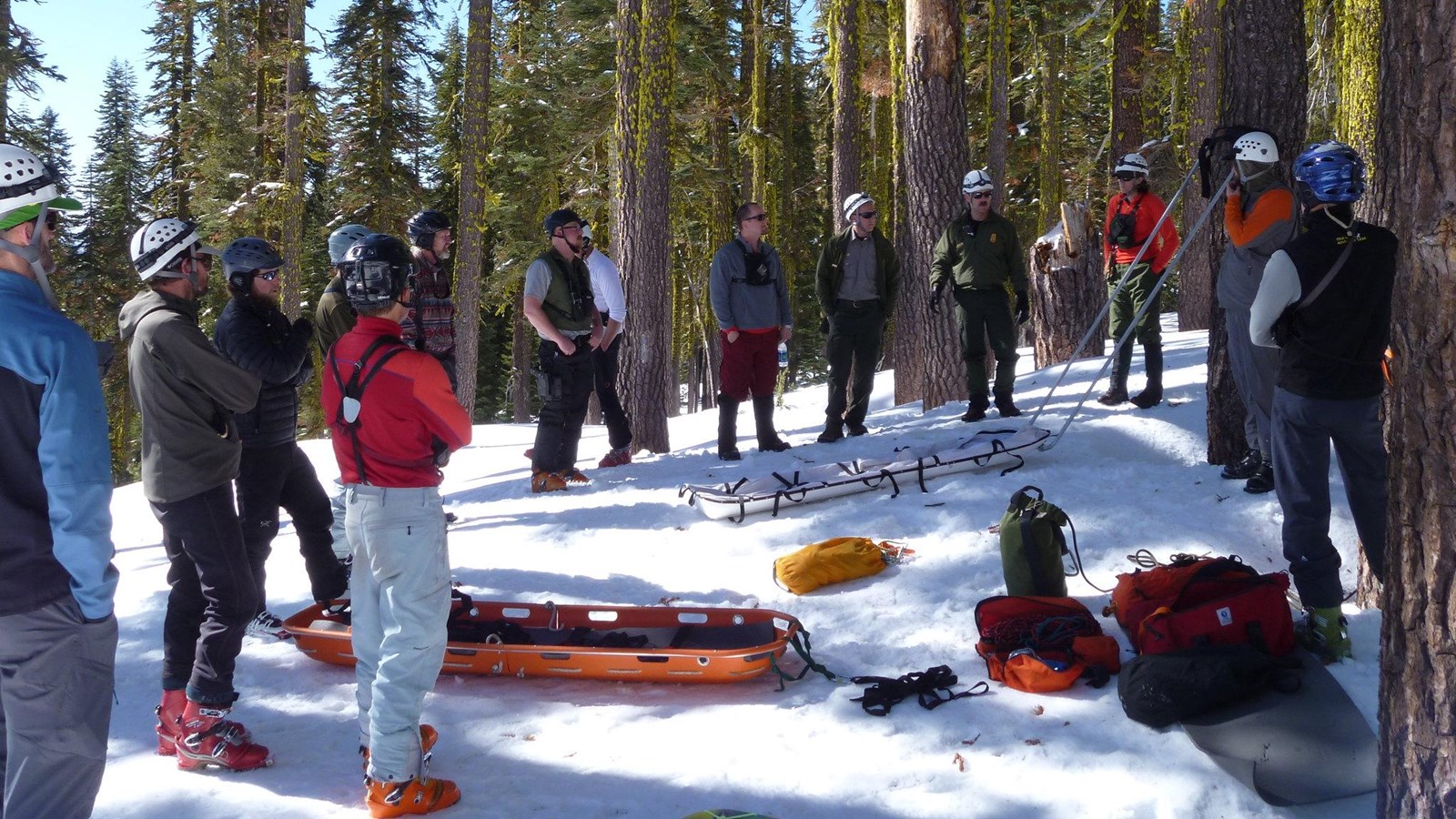 a group stands around an orange litter on a snowy, shady slope