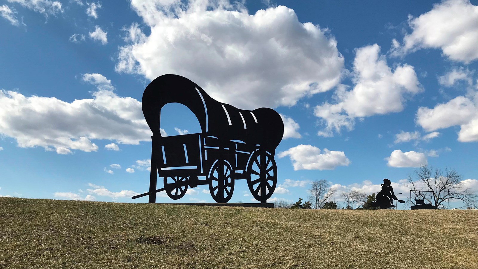 A wagon cut-out sits on the top of a grassy hill.