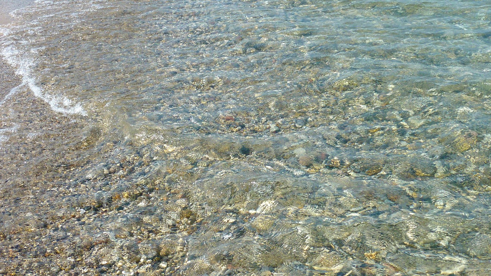 Crystal clear water at shore shimmers over white pebbly rocks