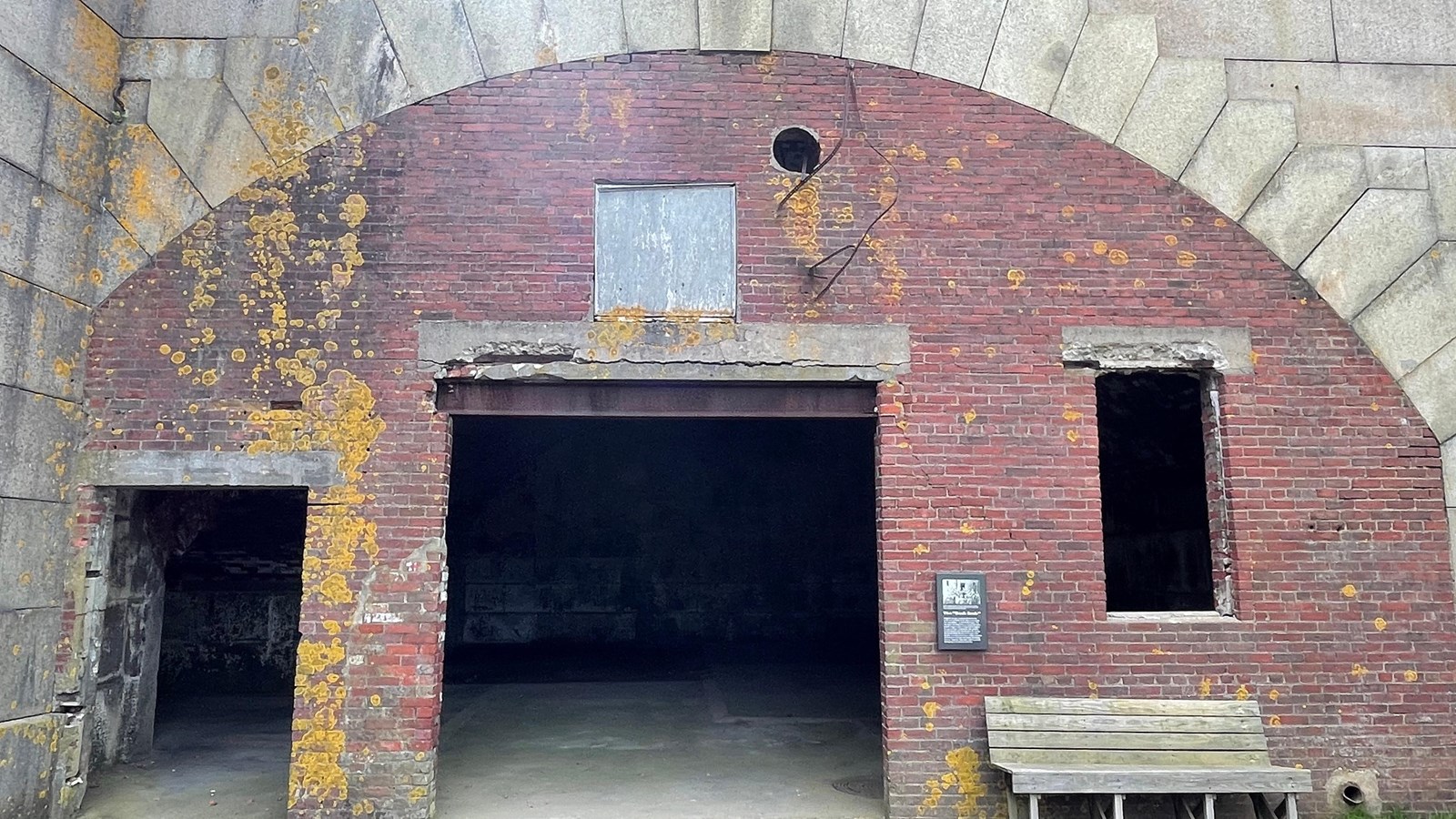 A stone wall with two brick surrounded entrances and a window.