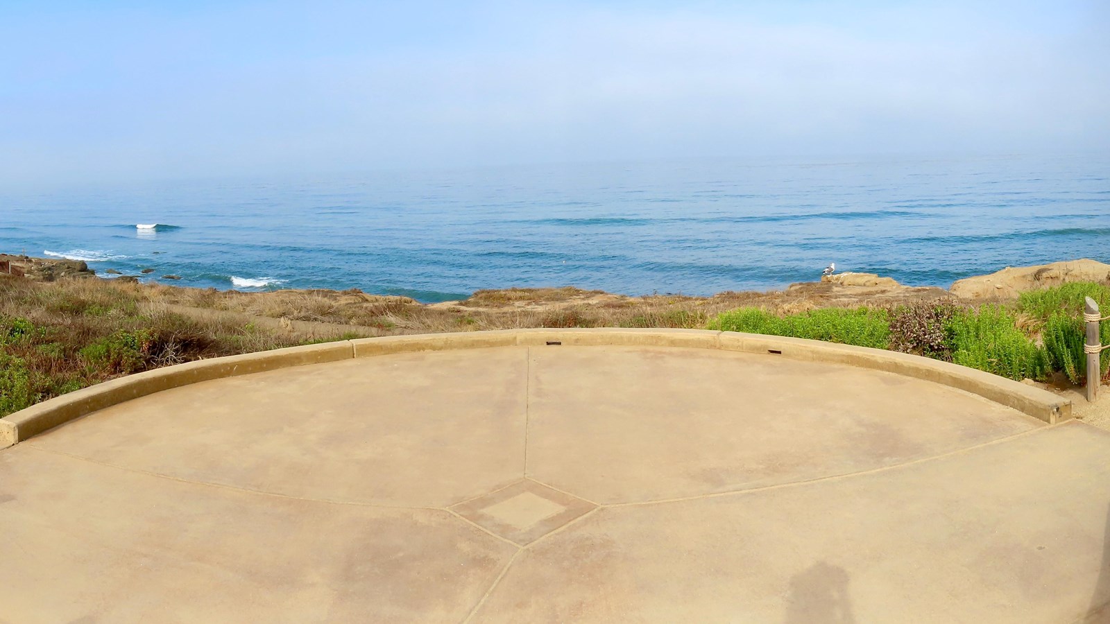A tan concrete circle allowing for ADA access overlooks the ocean. 