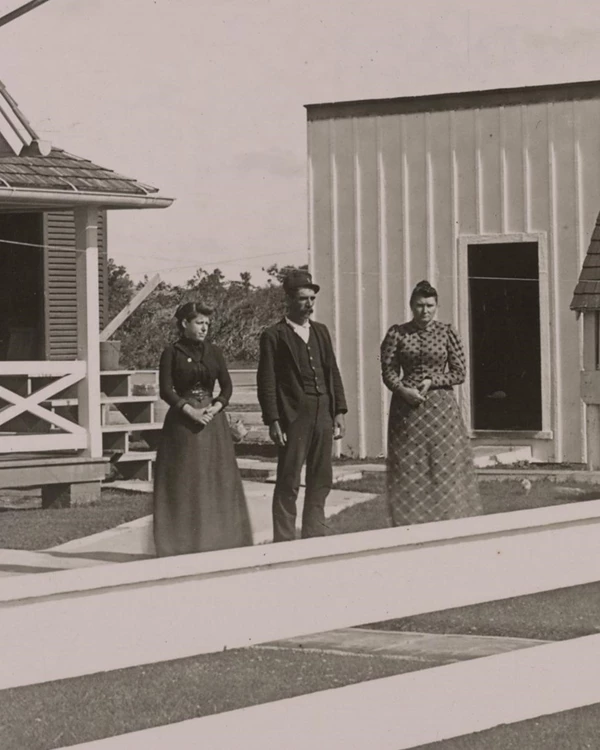 Black and white image of a lightkeeper and two women standing in a yard.