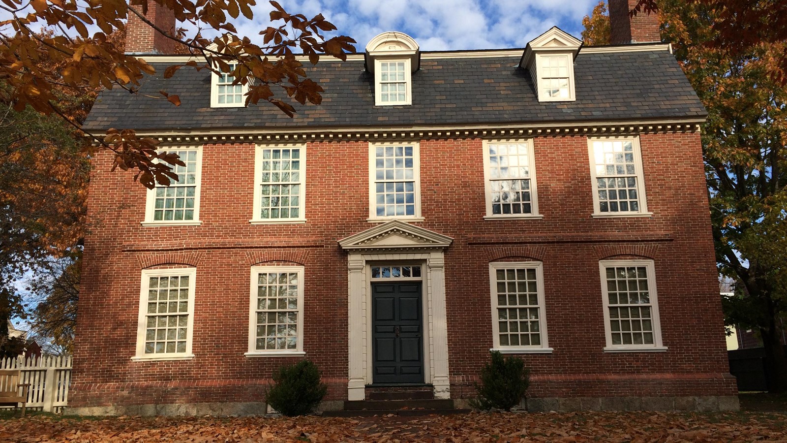 Three-story brick home with brick walkway leading to a green front door