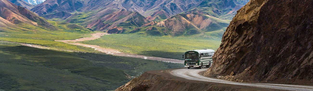 a green colored bus traveling a dirt road on a mountainside