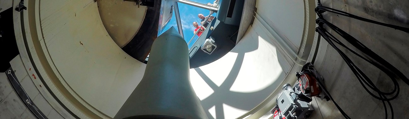 Park ranger and visitors look through a glass barrier at a missile standing in a missile silo