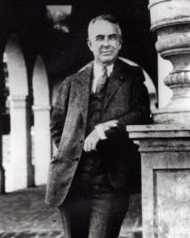 Man in suit leans against pole and poses for picture.