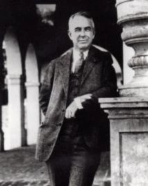 Man in suit leans against pole and poses for picture.