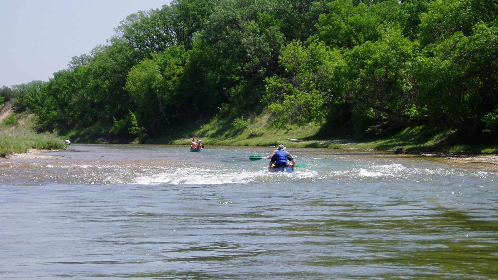 Waters rush over and through shallow rock edges in a chute which a kayaker floats down.