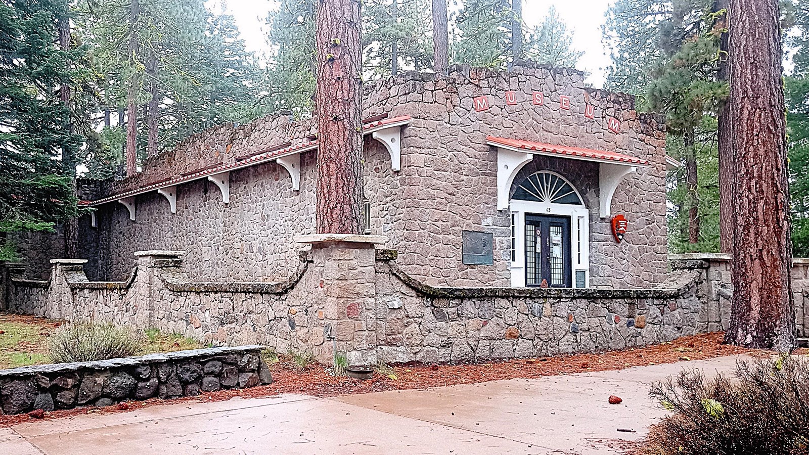 A one-story stone building surrounded by a short stone wall.