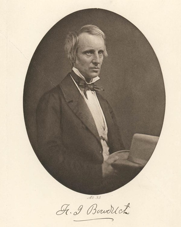 Black and white portrait of a White man with light hair wearing a dark suit and sitting at a desk.