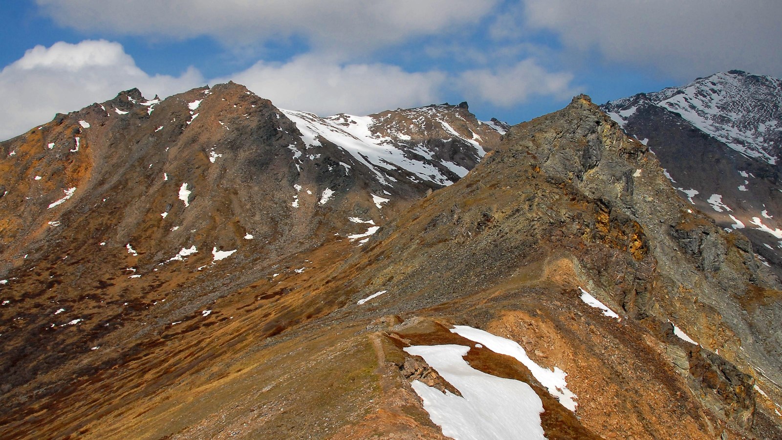 A jagged ridgeline with orange and red rocks and patches of snow.