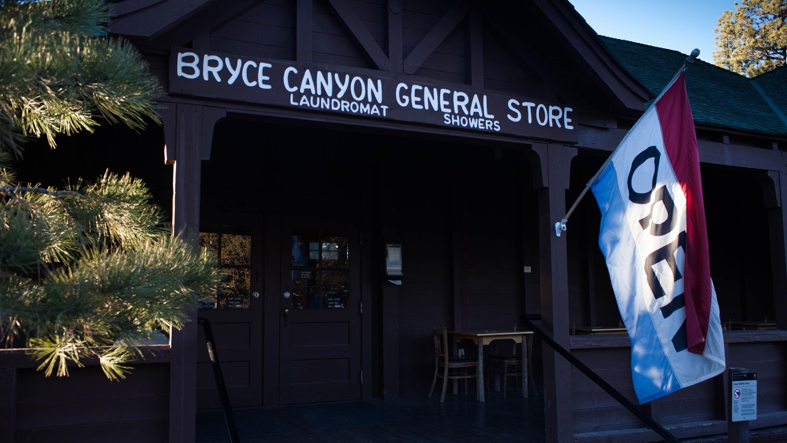 A brown wood porch with large Open flag; sign reads Bryce Canyon General Store Laundromat Showers