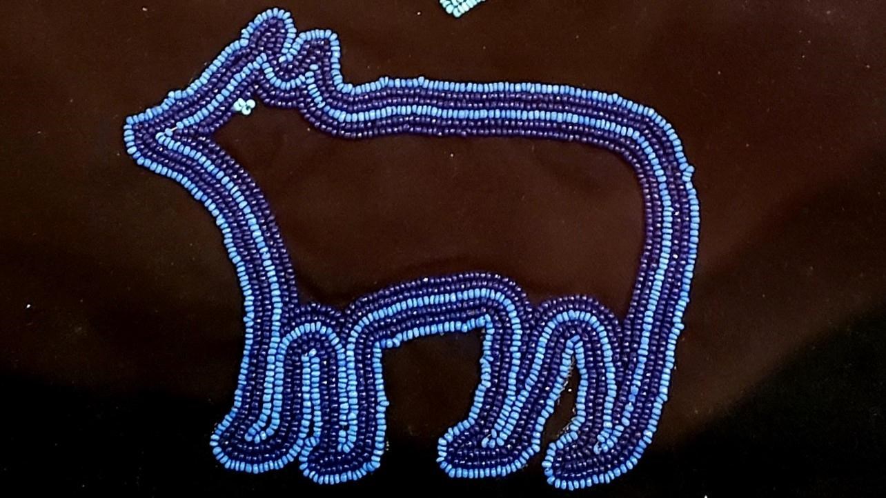 Beaded bag with a blue outline of a bear and orange six pointed star above.