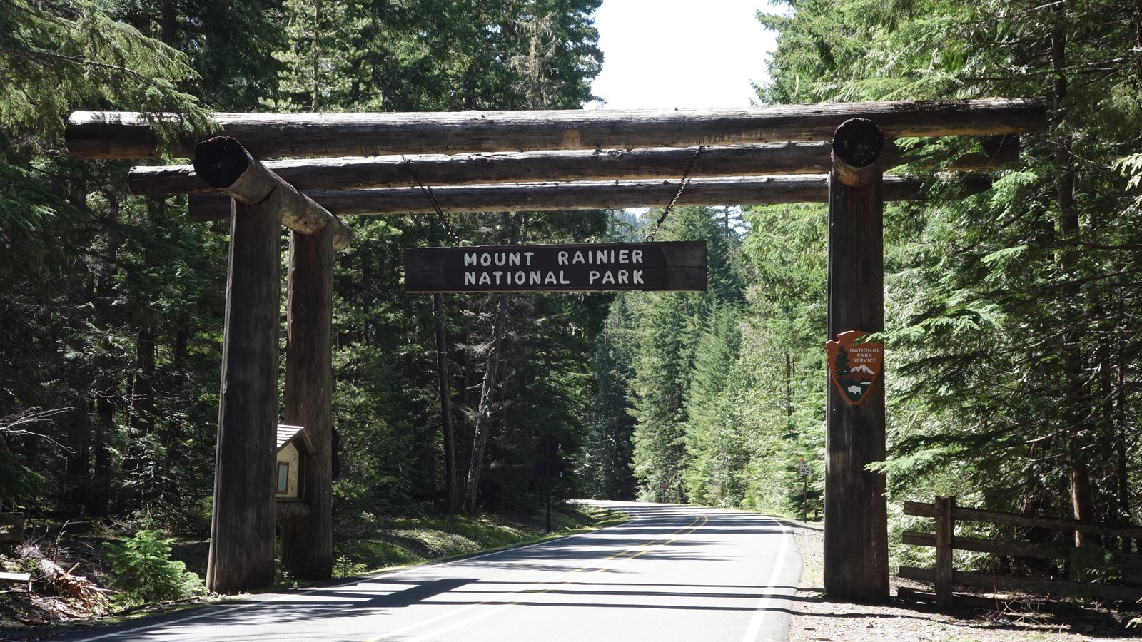 A two lane road leads through a large archway constructed of massive cedar logs.