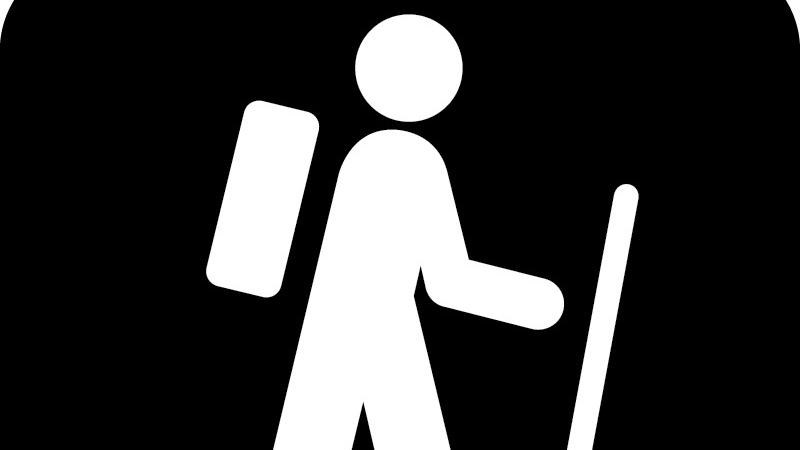 A symbol of a hiker wearing a backpack, using a walking stick, with a black background.