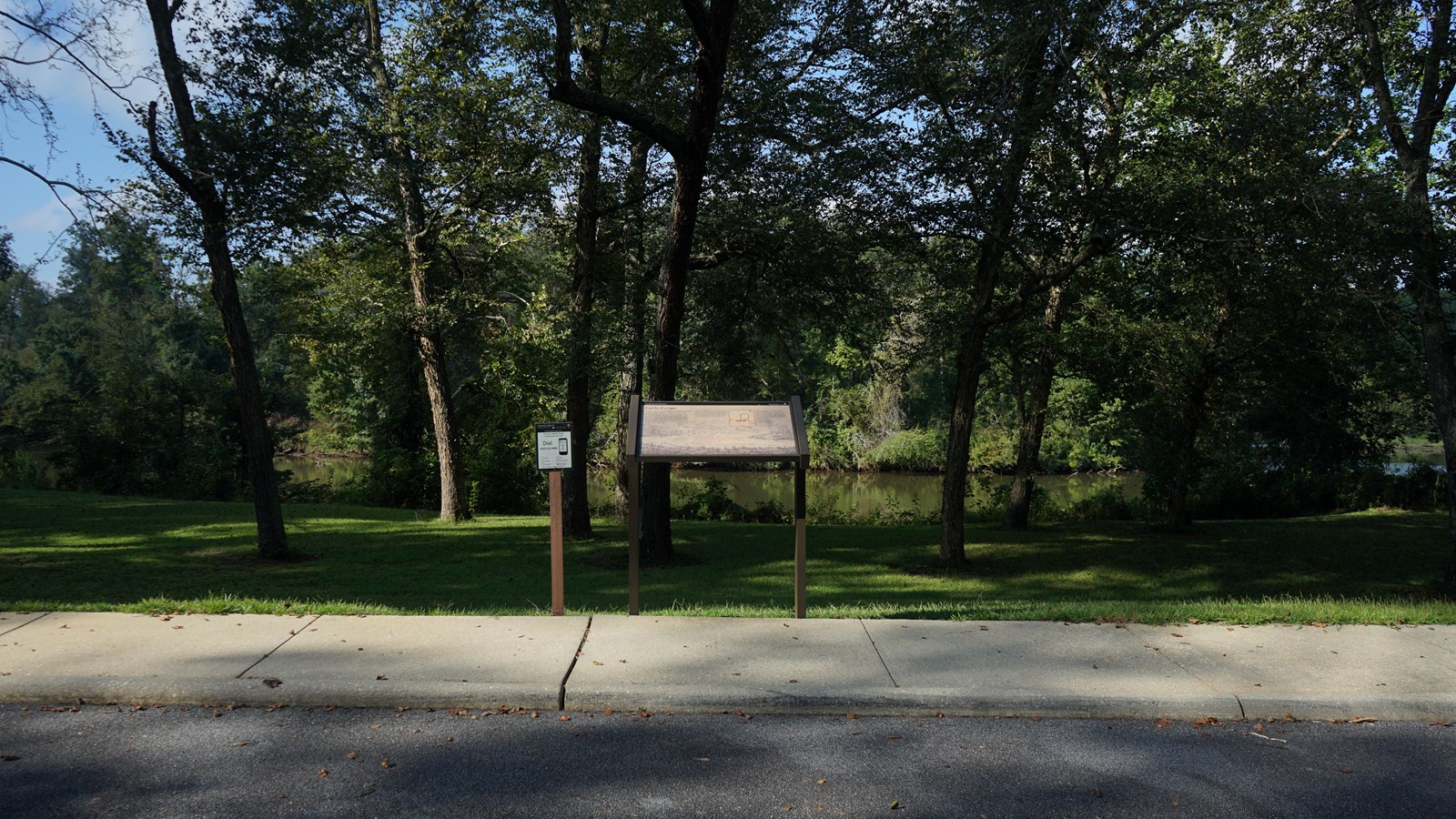 Image displays an informational wayside surrounded by grass, next to a river.