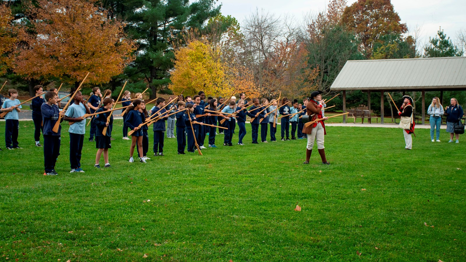 children lined up holding wooden muskets in front of park rangers wearing soldier uniforms