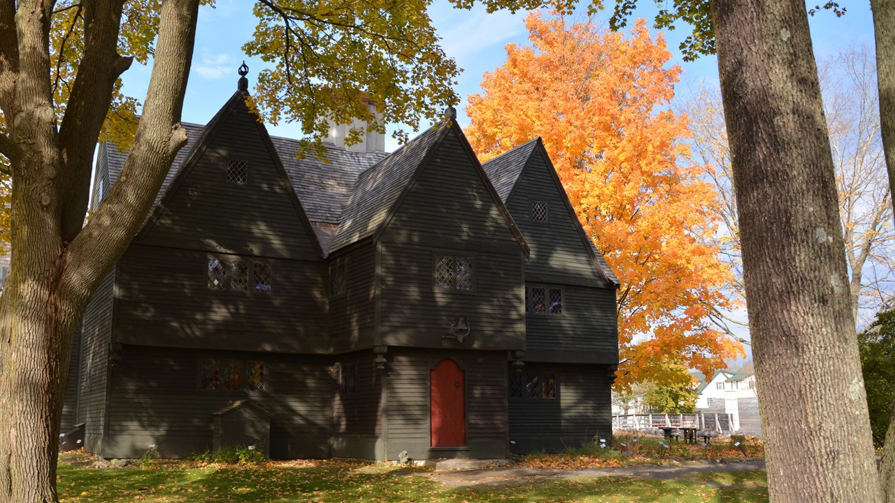 Large gray three story building with red door surrounded by green and yellow trees.