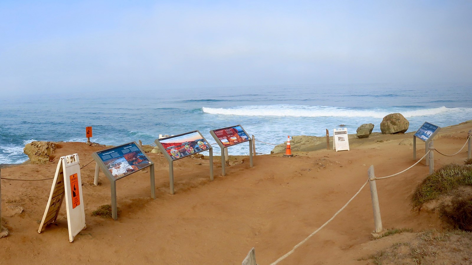 Three waysides to the left of a dirt path. Blue ocean in background.