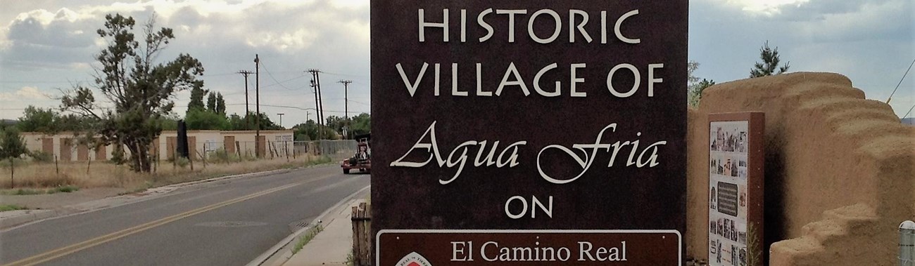 A historic 1640 village of agua fria wooden sign sits next to a road.