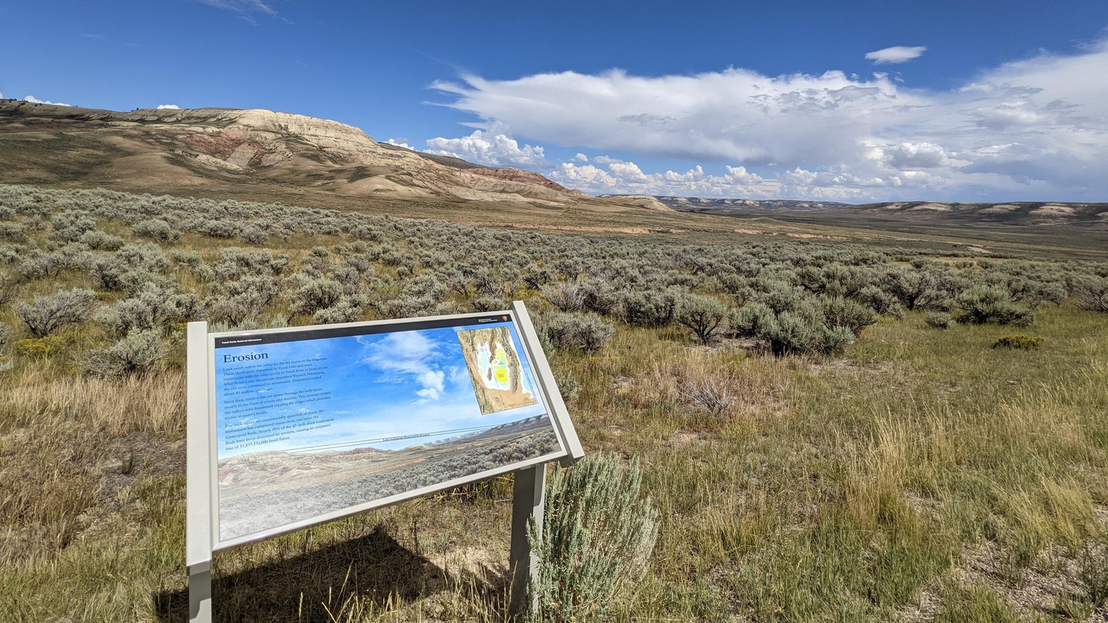 A low angled sign with the title Erosion. Behind is the butte and a ridgeline across the valley.
