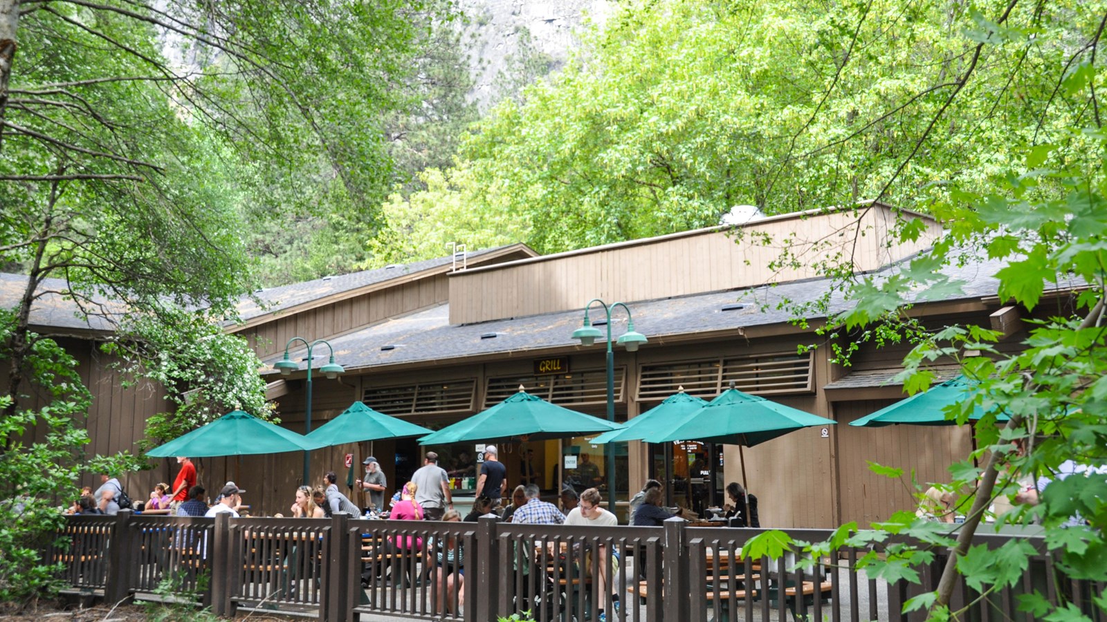 People eating at outdoor seating with umbrellas on the deck of the grill