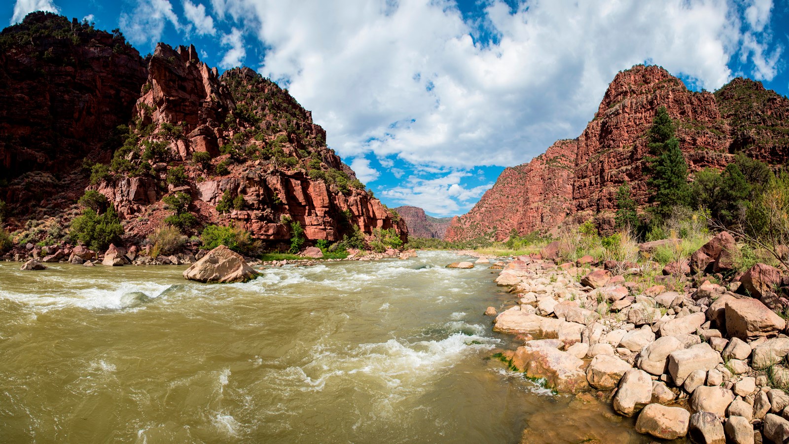 A fast flowing river, rushing through a steep, reddish desert canyon.